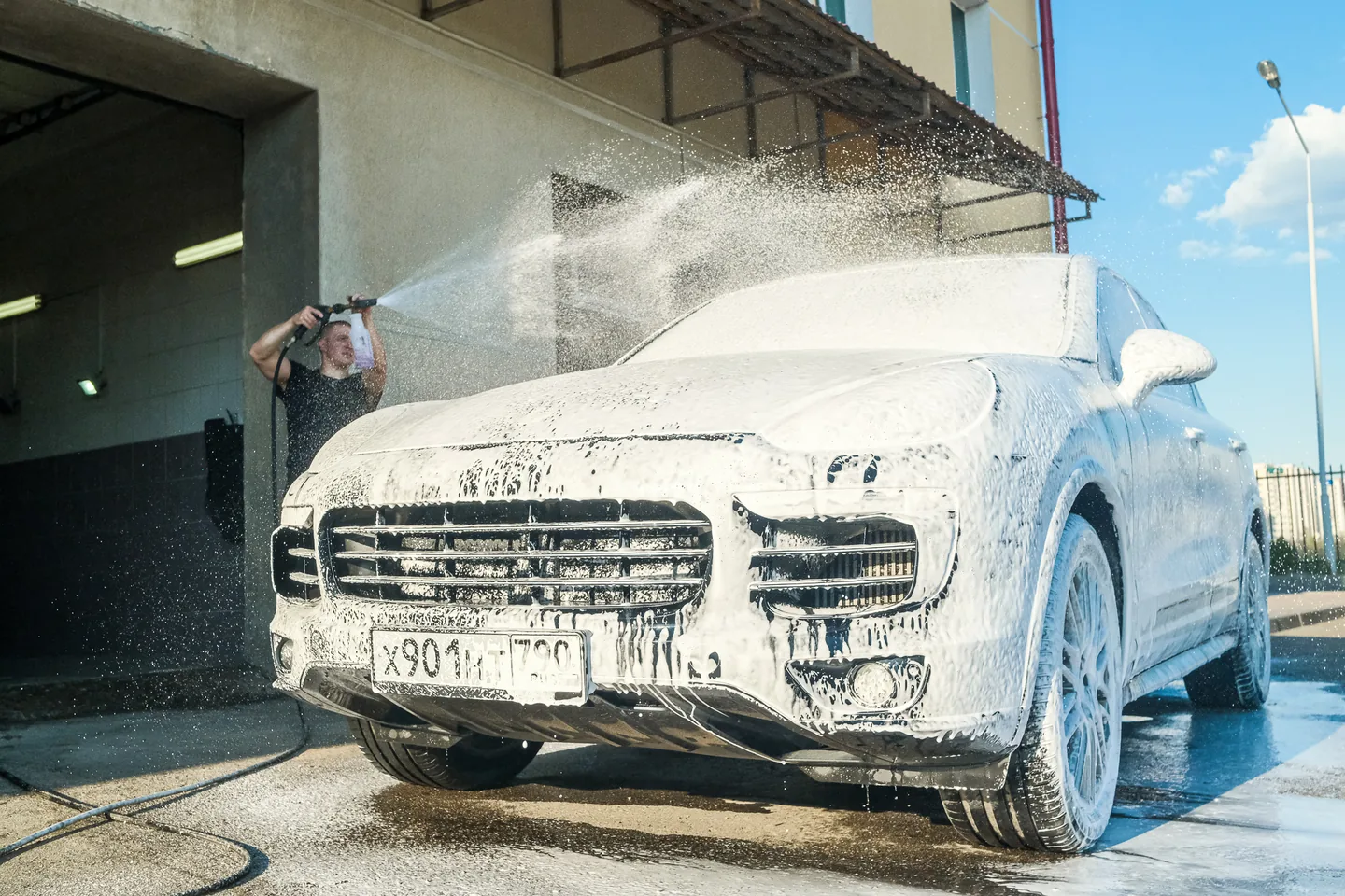 Мастер смывает пену с Porsche Cayenne у ворот бокса
